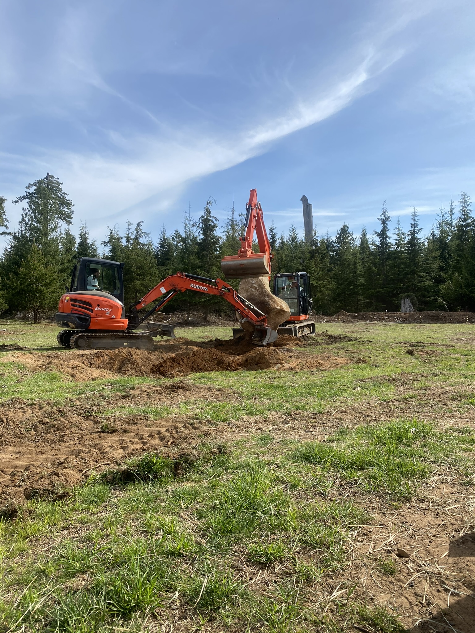 Two Kubota excavators working in a field, lifting boulders on Vancouver Island